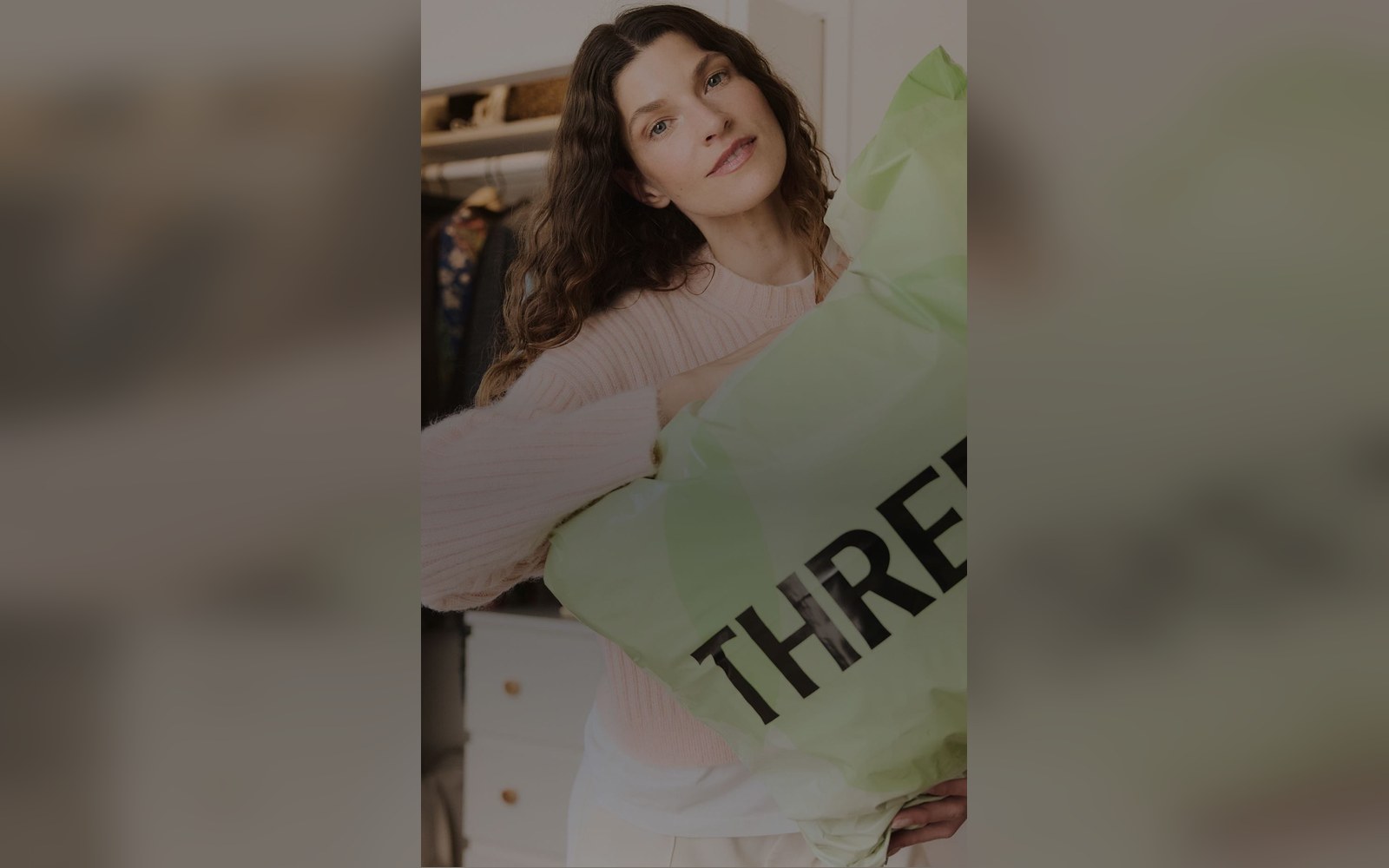 Woman holds a large green ThredUp shipping bag while standing in a closet